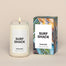 A lit Surf Shack Homesick candle displayed next to its boxed packaging on a dark cream background.