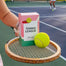 The boxed Tennis League called displayed on an old school tennis racket with a tennis ball next to it. The blurred tennis court is the background.