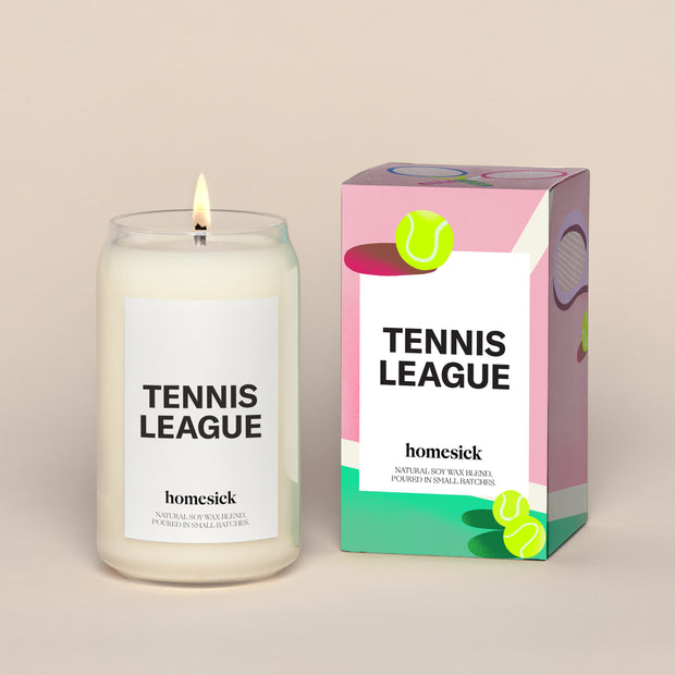 A lit Tennis League  Homesick candle displayed next to its boxed packaging on a dark cream background.
