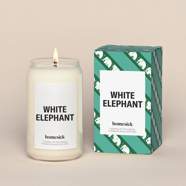 A lit White Elephant Homesick candle displayed next to its boxed packaging on a dark cream background.
