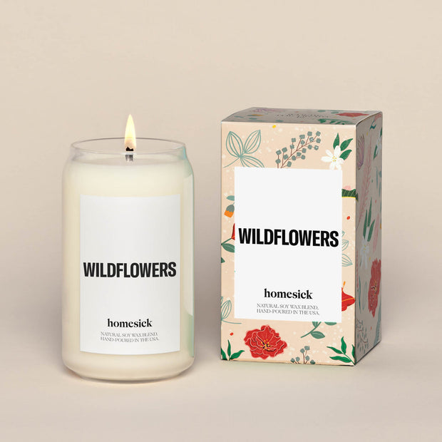 A lit Wildflower Homesick candle displayed next to its boxed packaging on a dark cream background.