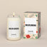 A lit Wildflower Homesick candle displayed next to its boxed packaging on a dark cream background.