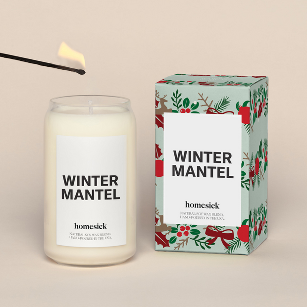 A lit Winter MantelHomesick candle displayed next to its boxed packaging on a dark cream background.