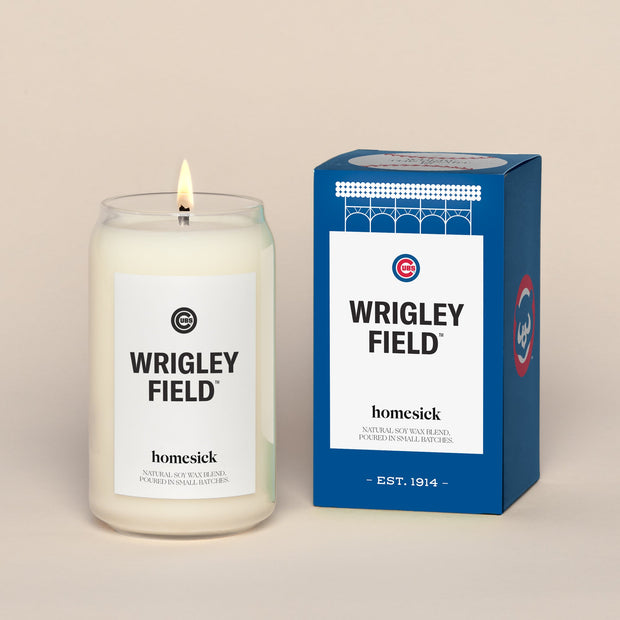 A lit Wrigley Field Homesick candle displayed next to its boxed packaging on a dark cream background.