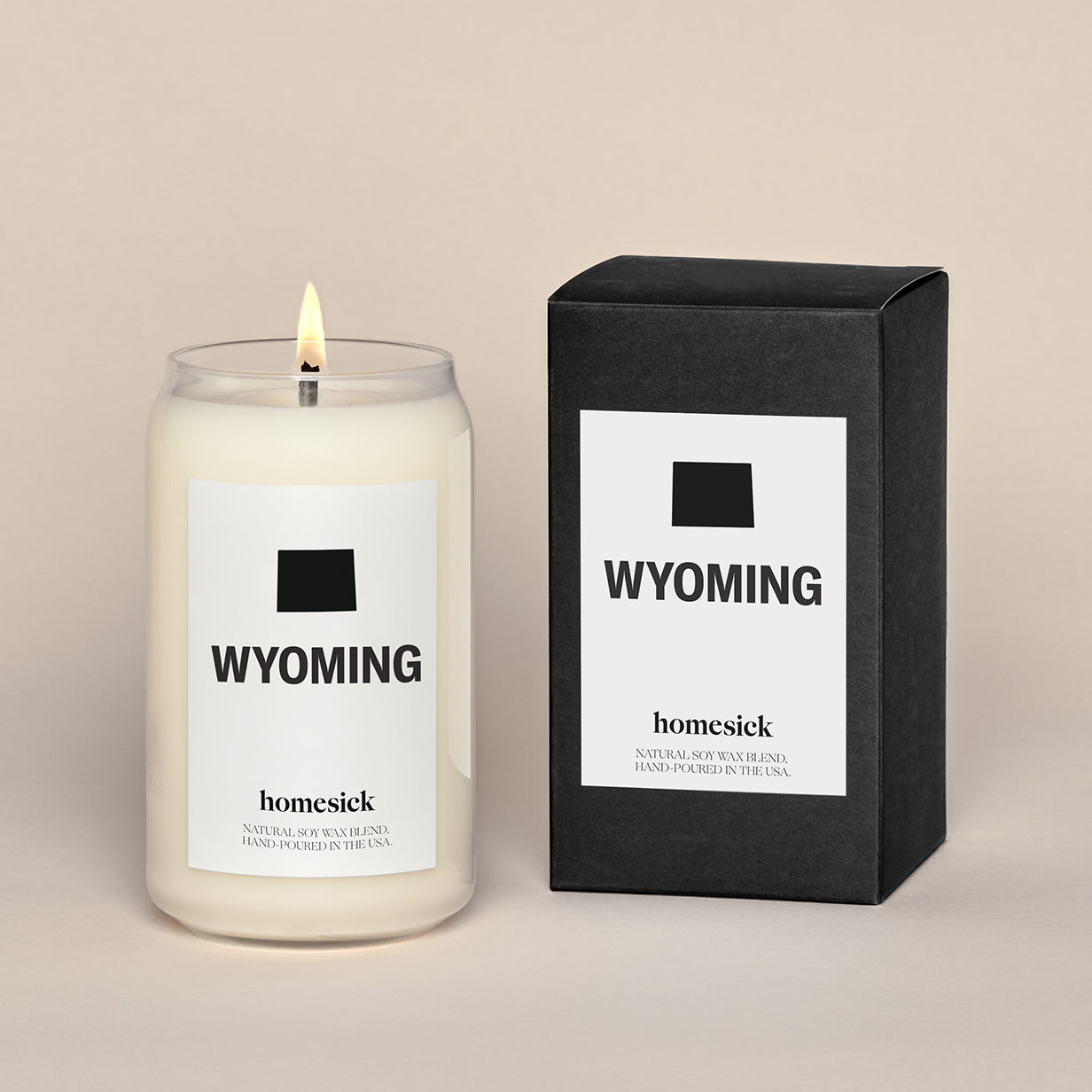 A lit Wyoming Homesick candle displayed next to its boxed packaging on a dark cream background.