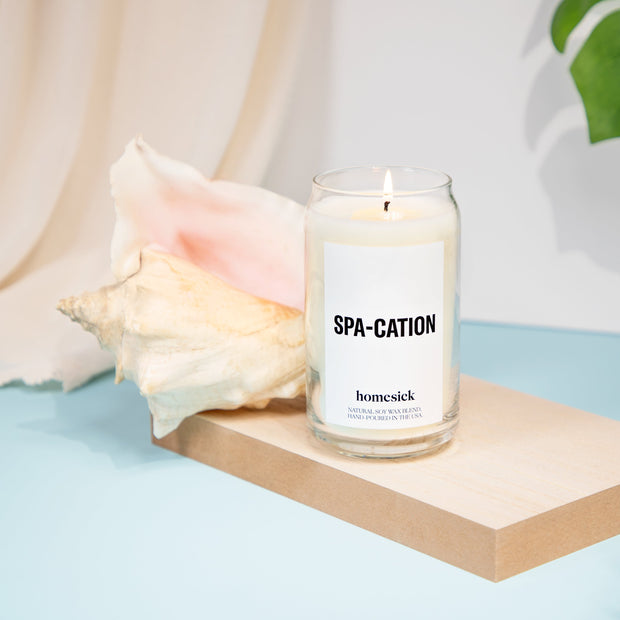 Single spa-cation candle next a large sea shell on relaxing background.